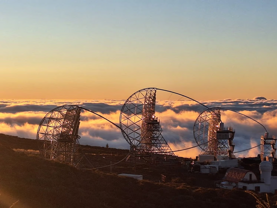 Three telescope dishes supported by oval frames and space frames behind them against the clouds